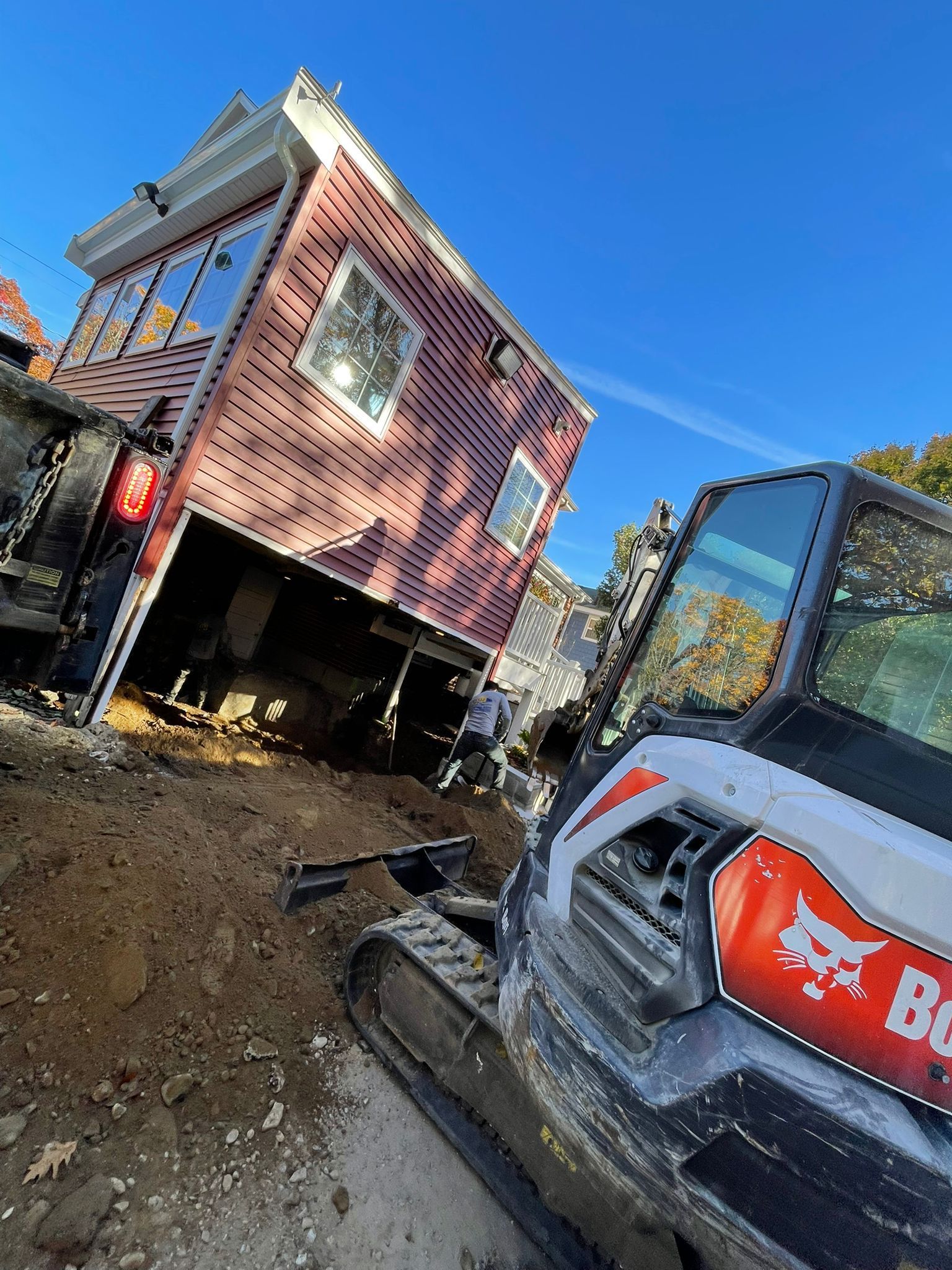 A bobcat excavator is sitting next to a house that is being moved.