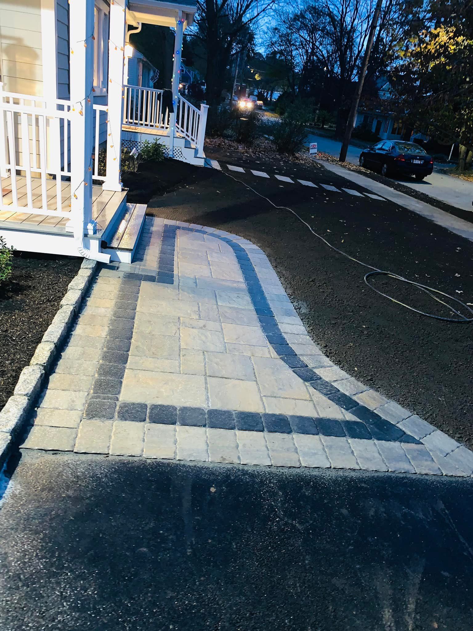 A walkway leading to a house with a car parked on the side of the road.