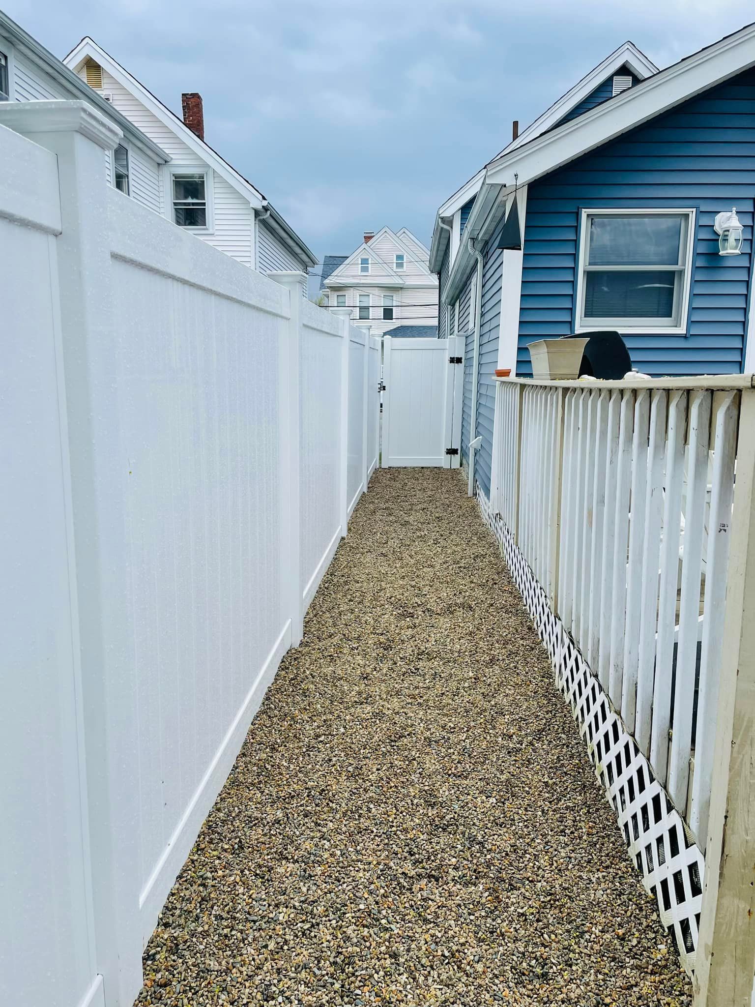 A white fence along a gravel path between two houses.