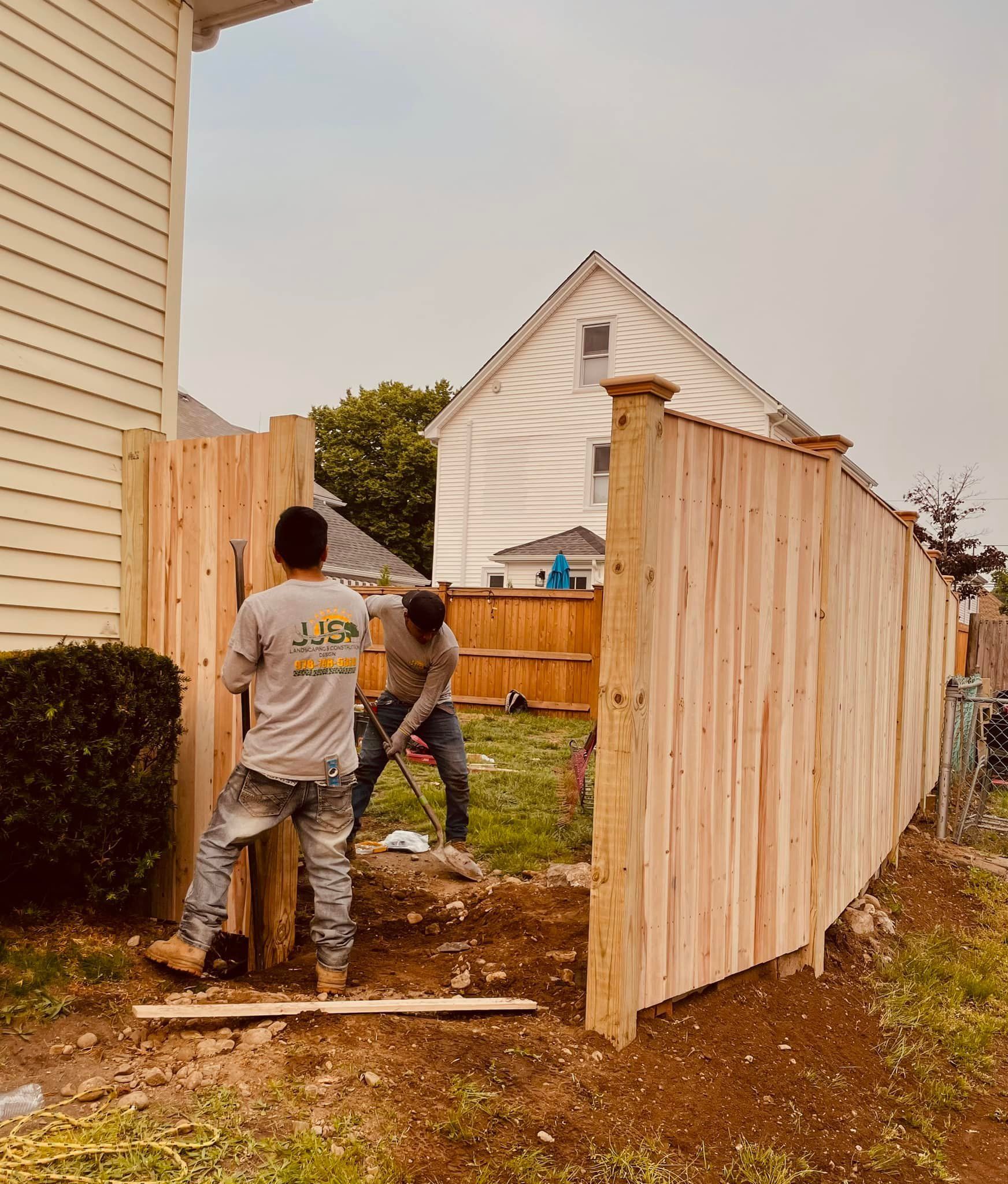 Two men are working on a wooden fence in front of a house.