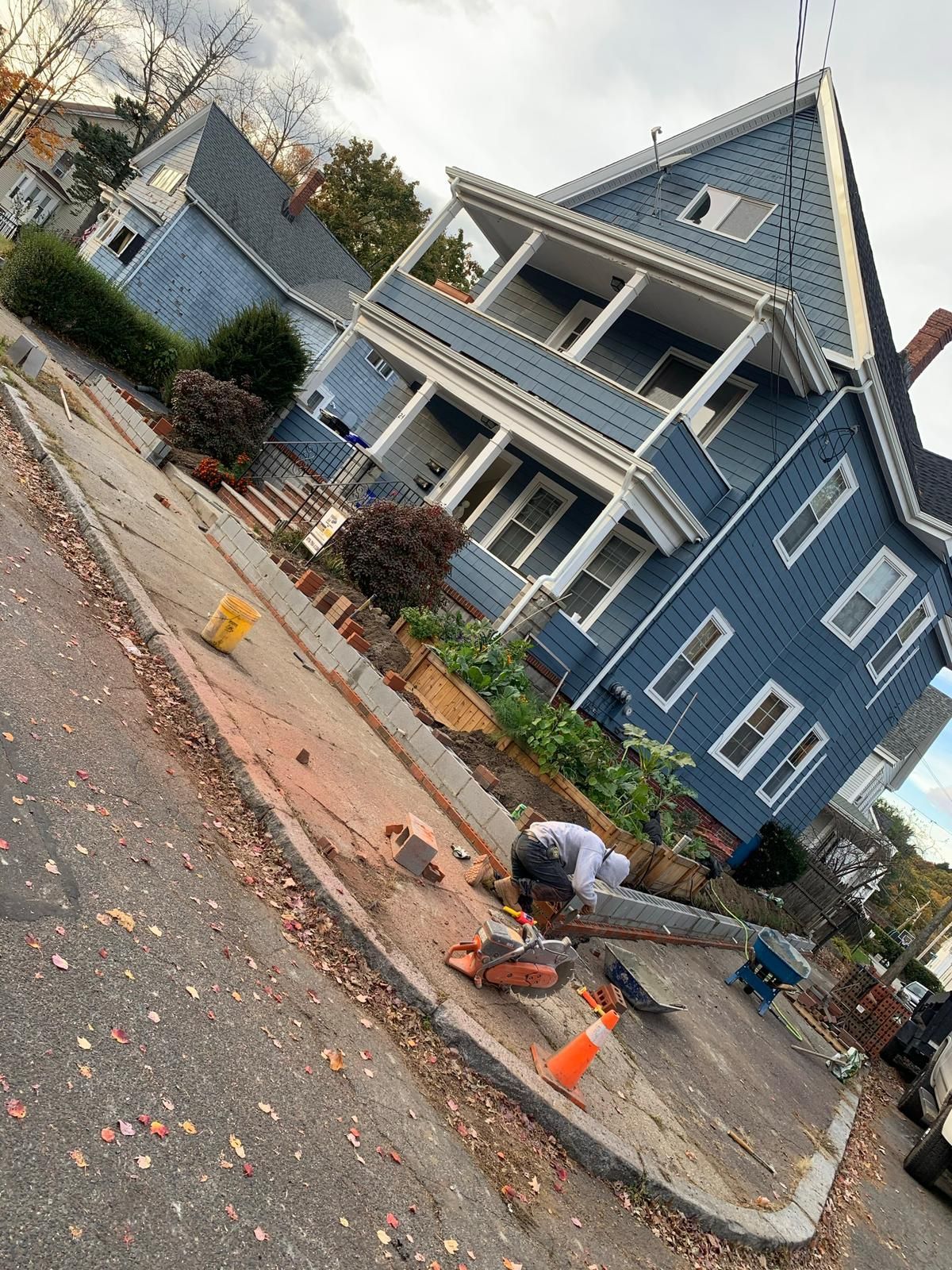 A man is working on a sidewalk in front of a blue house.