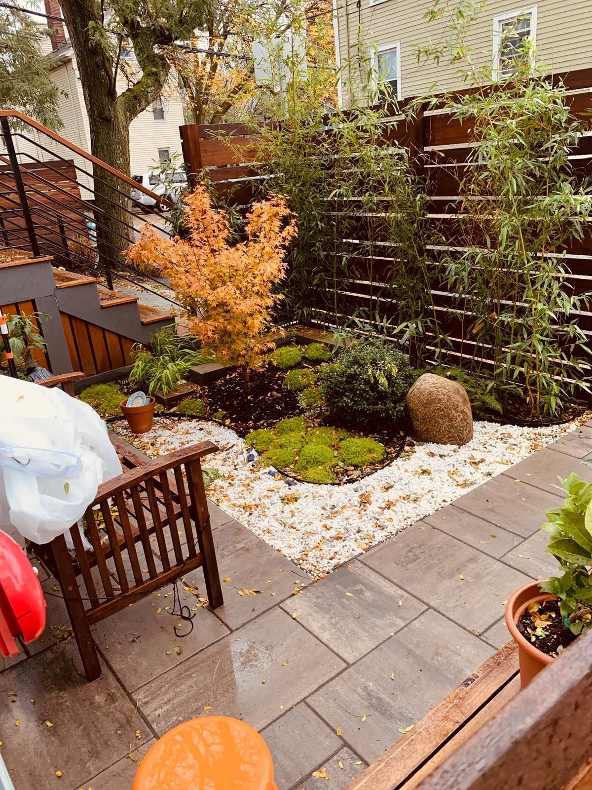 A patio with a wooden bench and a fence surrounded by plants and rocks.