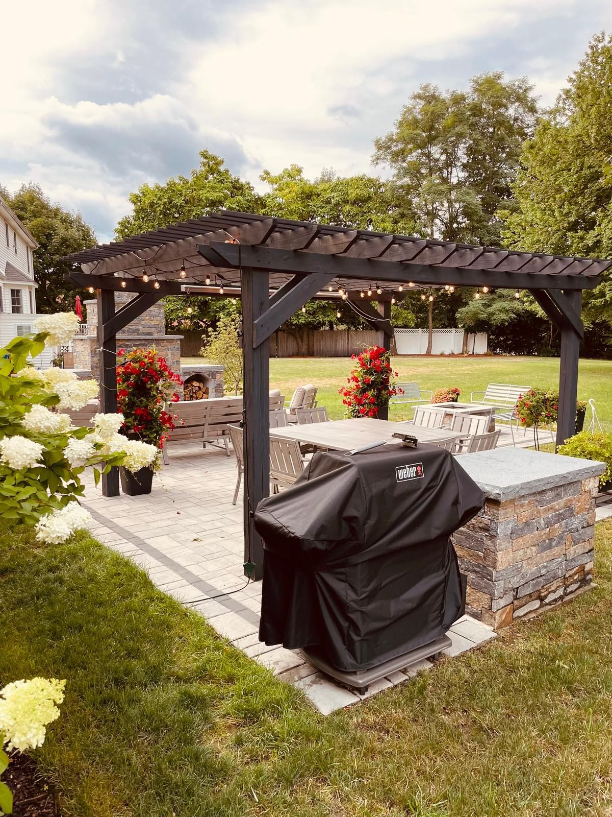 There is a grill under a pergola in the backyard.