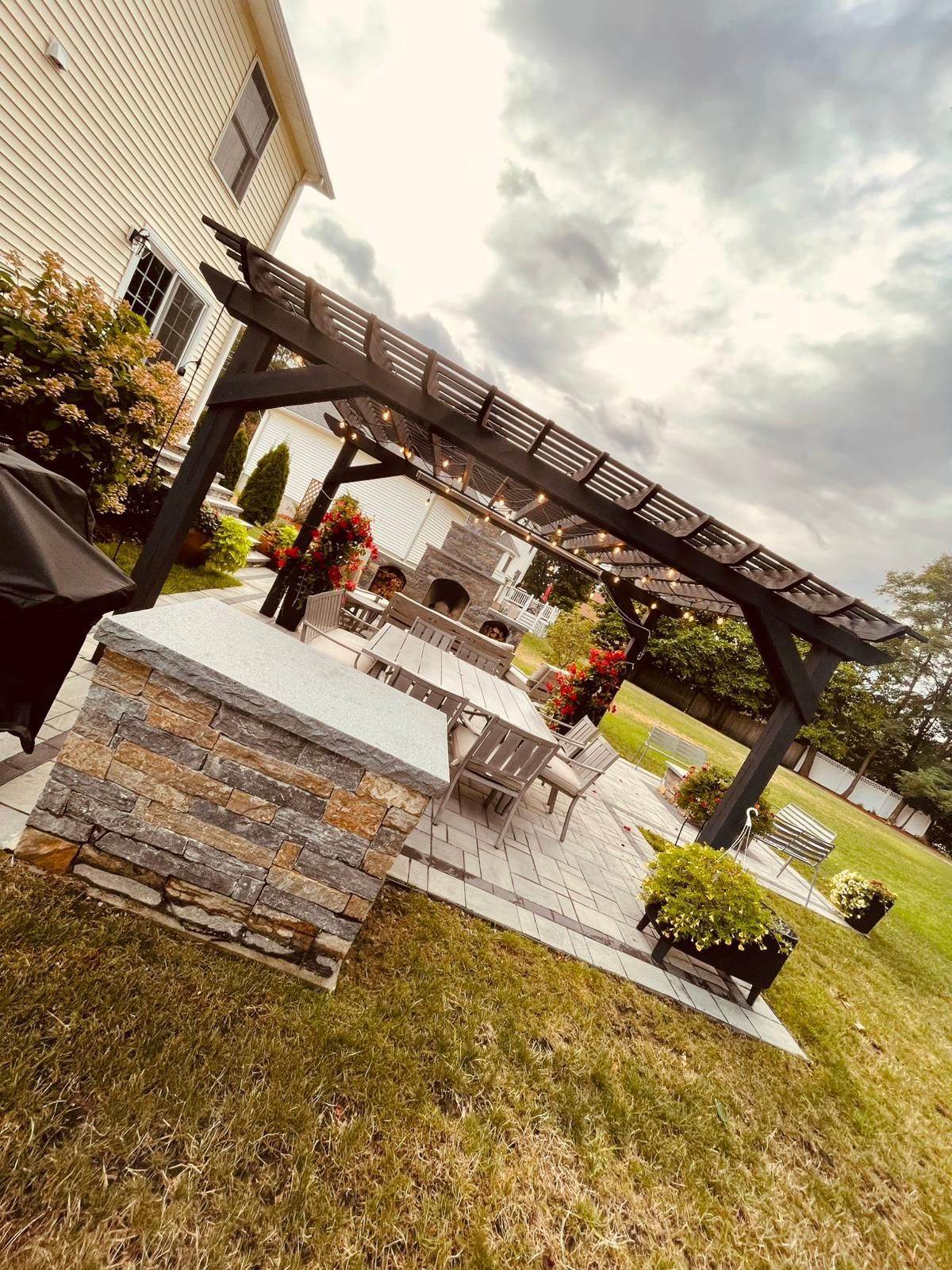 There is a pergola in the backyard with a table and chairs underneath it.