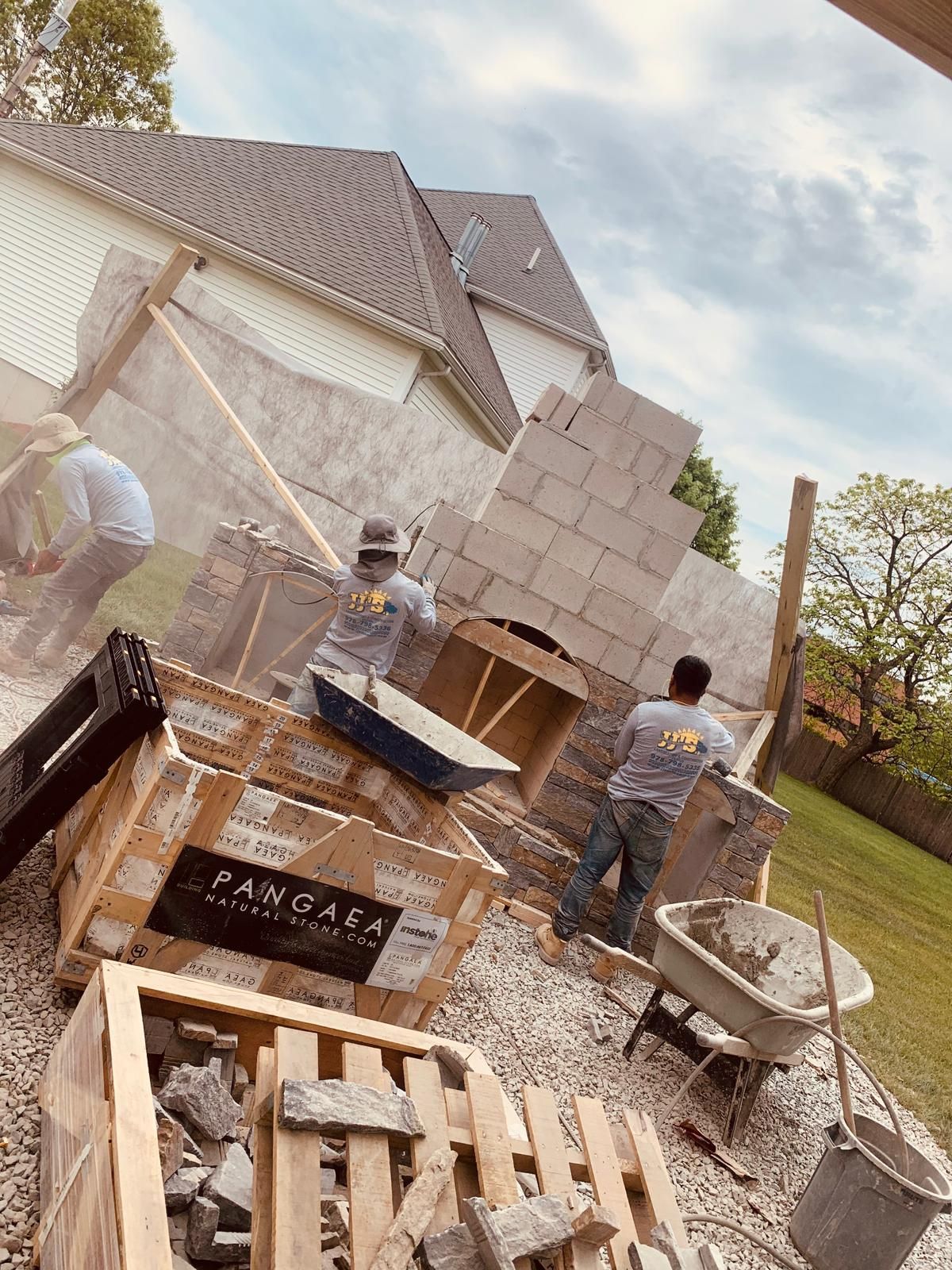 A group of men are working on a brick fireplace in a backyard.