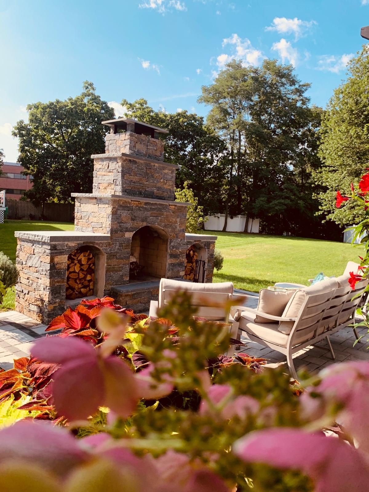 There is a fireplace in the backyard with a couch and chairs in the background.