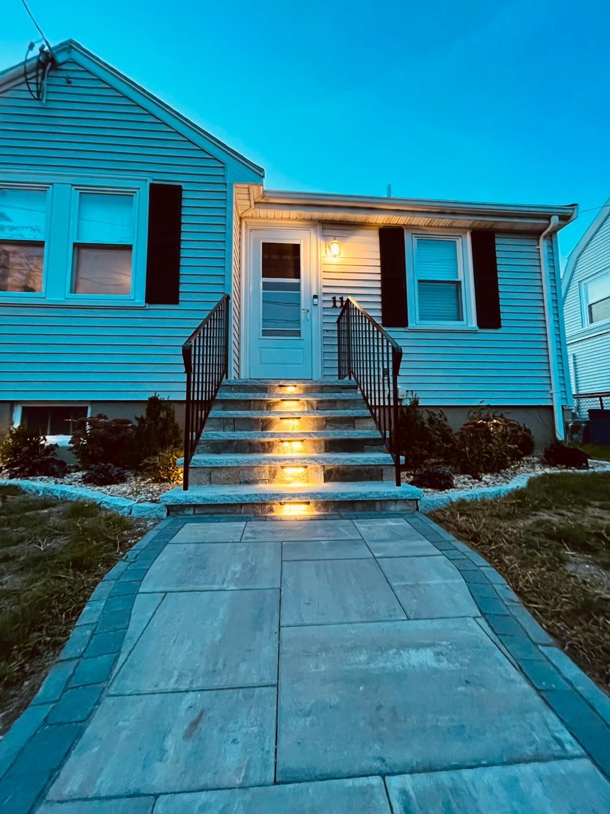 A house with stairs leading up to the front door is lit up at night.
