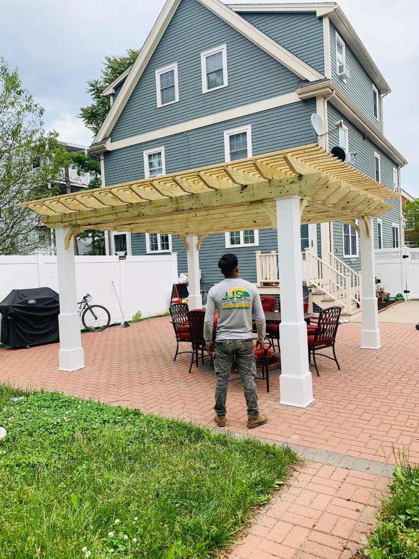 A man is standing under a wooden pergola in front of a house.