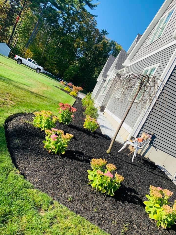 A house with a lot of flowers and mulch in front of it.