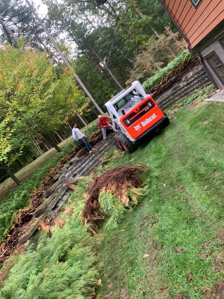 A bobcat is driving down a hill in a yard next to a house.