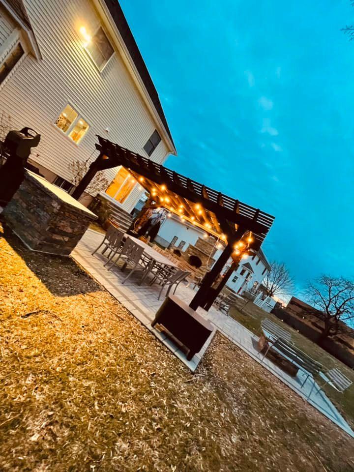 A pergola with lights hanging from it is in the backyard of a house.