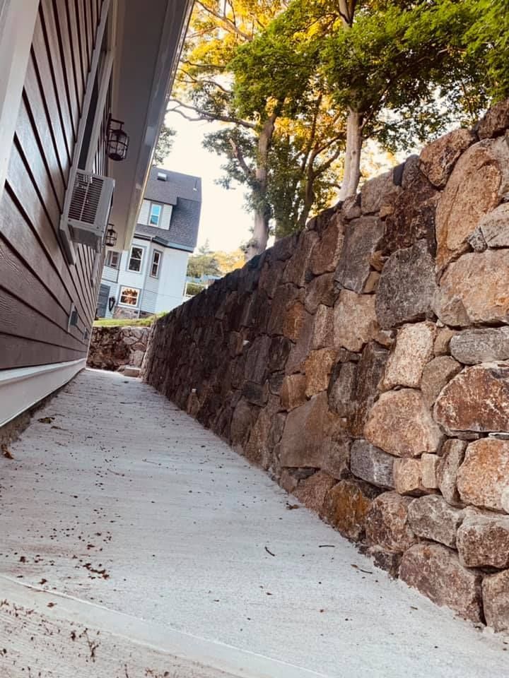 A stone wall along a sidewalk next to a house.