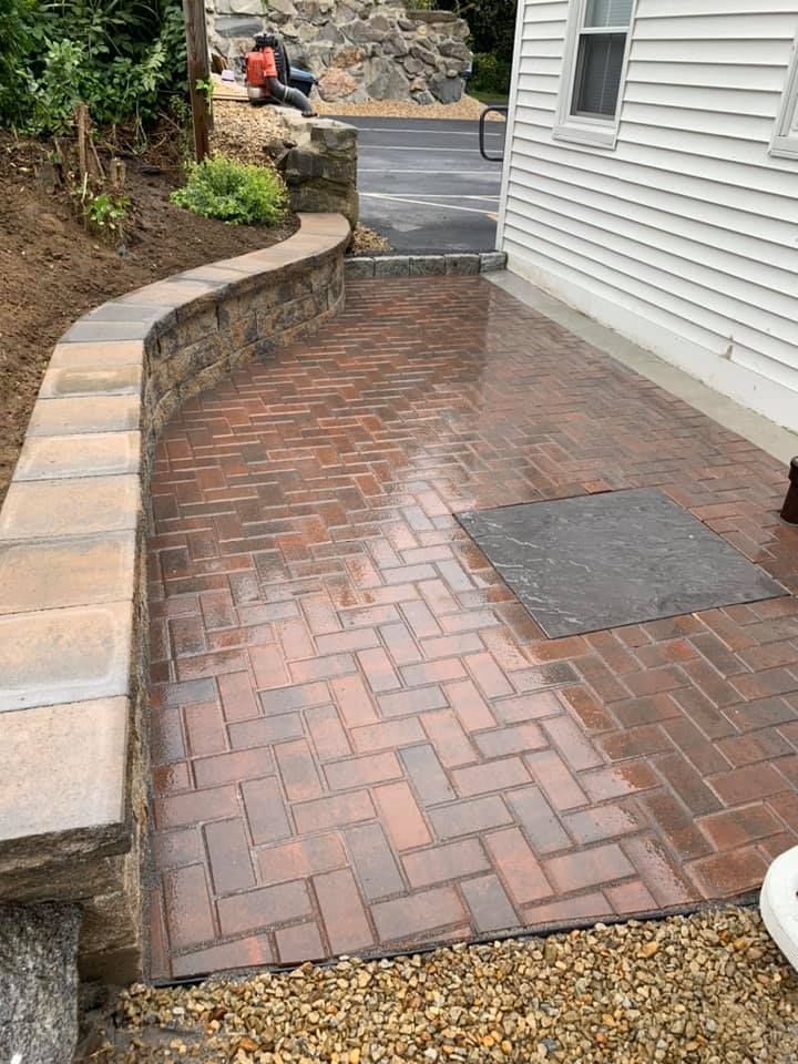 A brick walkway leading to a house with a stone wall.