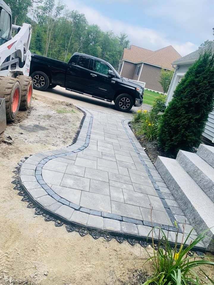 A black truck is parked on a sidewalk next to a bobcat.