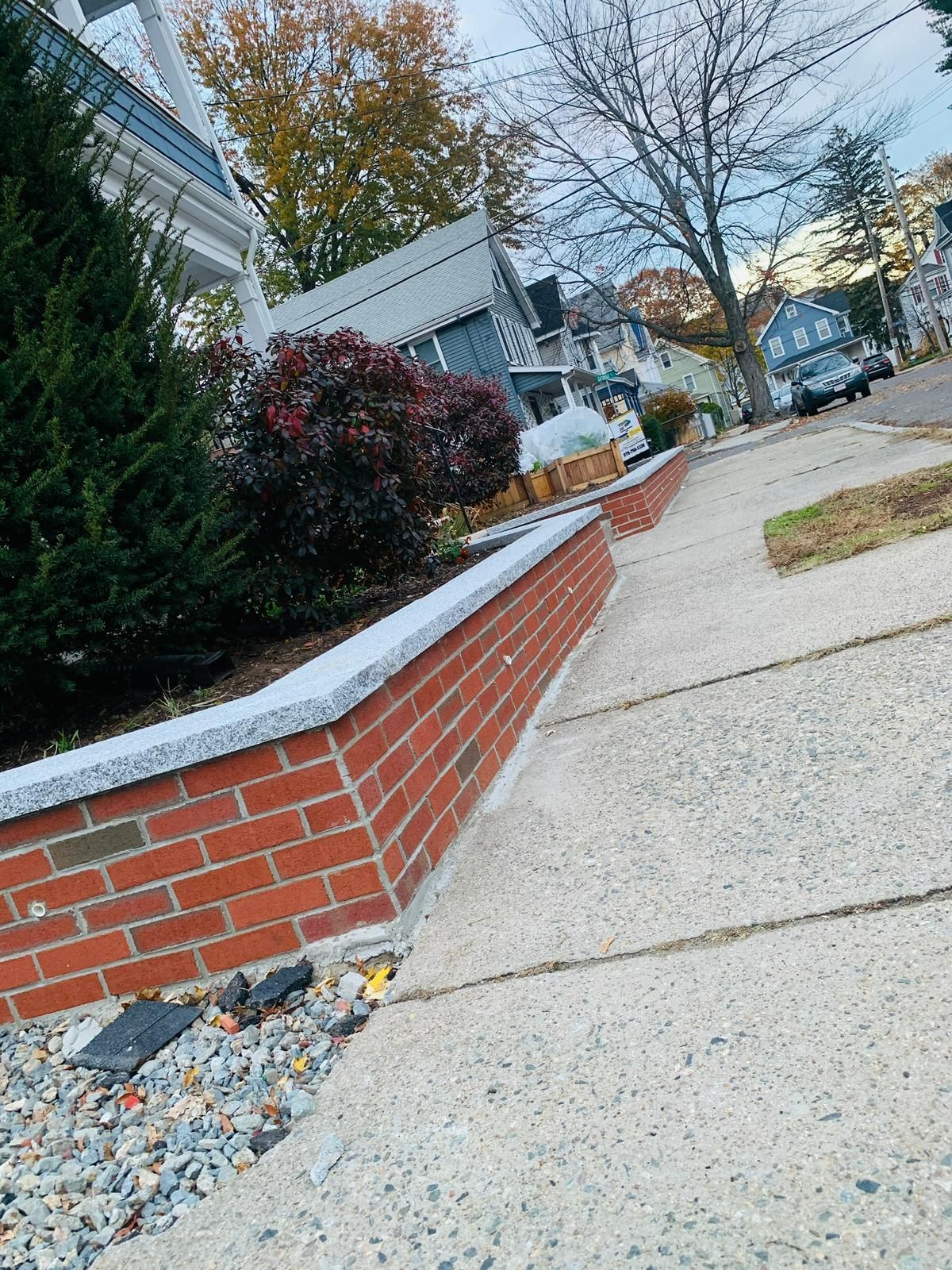 A brick wall on the side of a sidewalk next to a sidewalk.