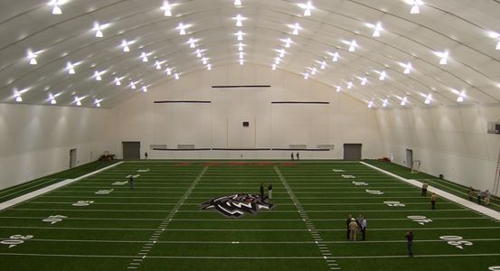 Indoor football field with artificial turf, under a domed white ceiling with bright lights.