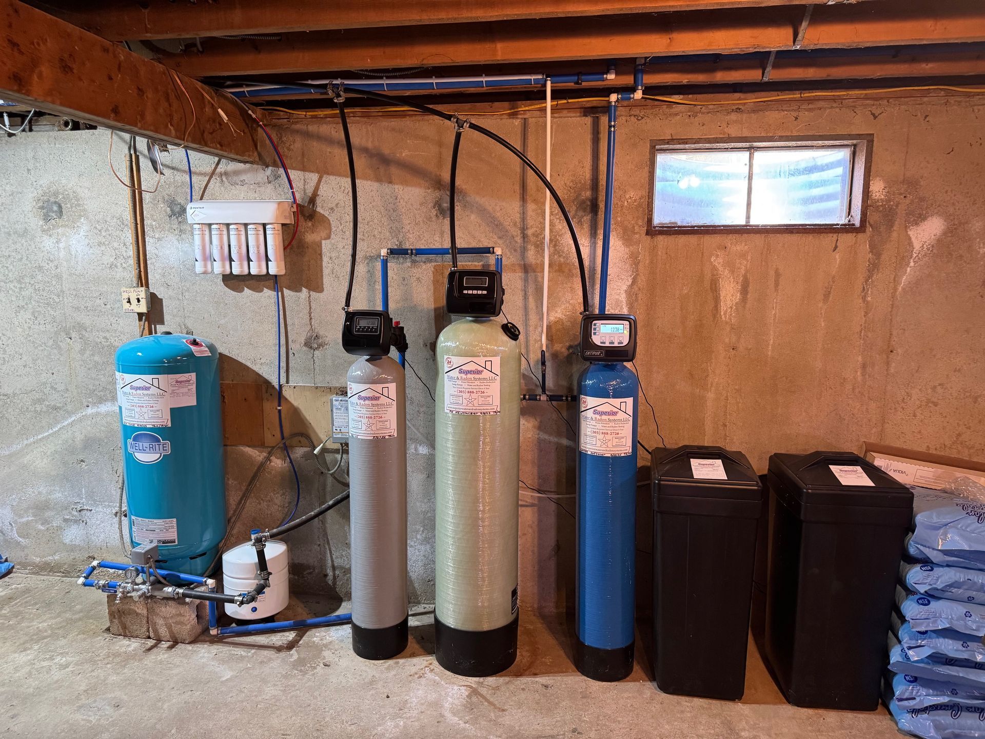 Water treatment equipment with blue and black filtration tanks and pipes in a basement utility room.