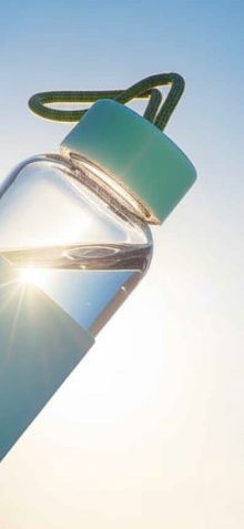 A close-up of a water bottle with a green lid against a blue sky.