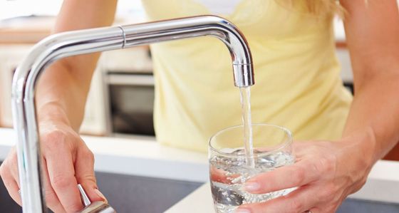 A woman is pouring water into a glass from a faucet