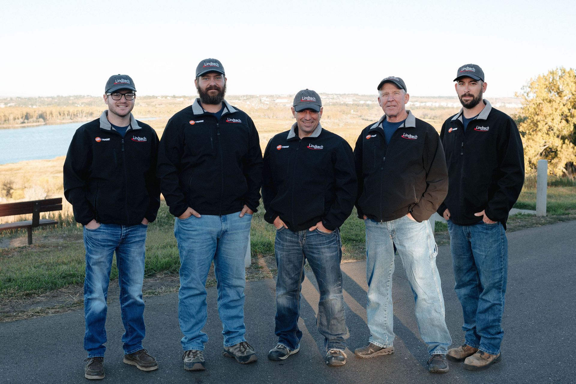 A group of men from Lindtech Services, Inc stands next to each other in front of a lake.