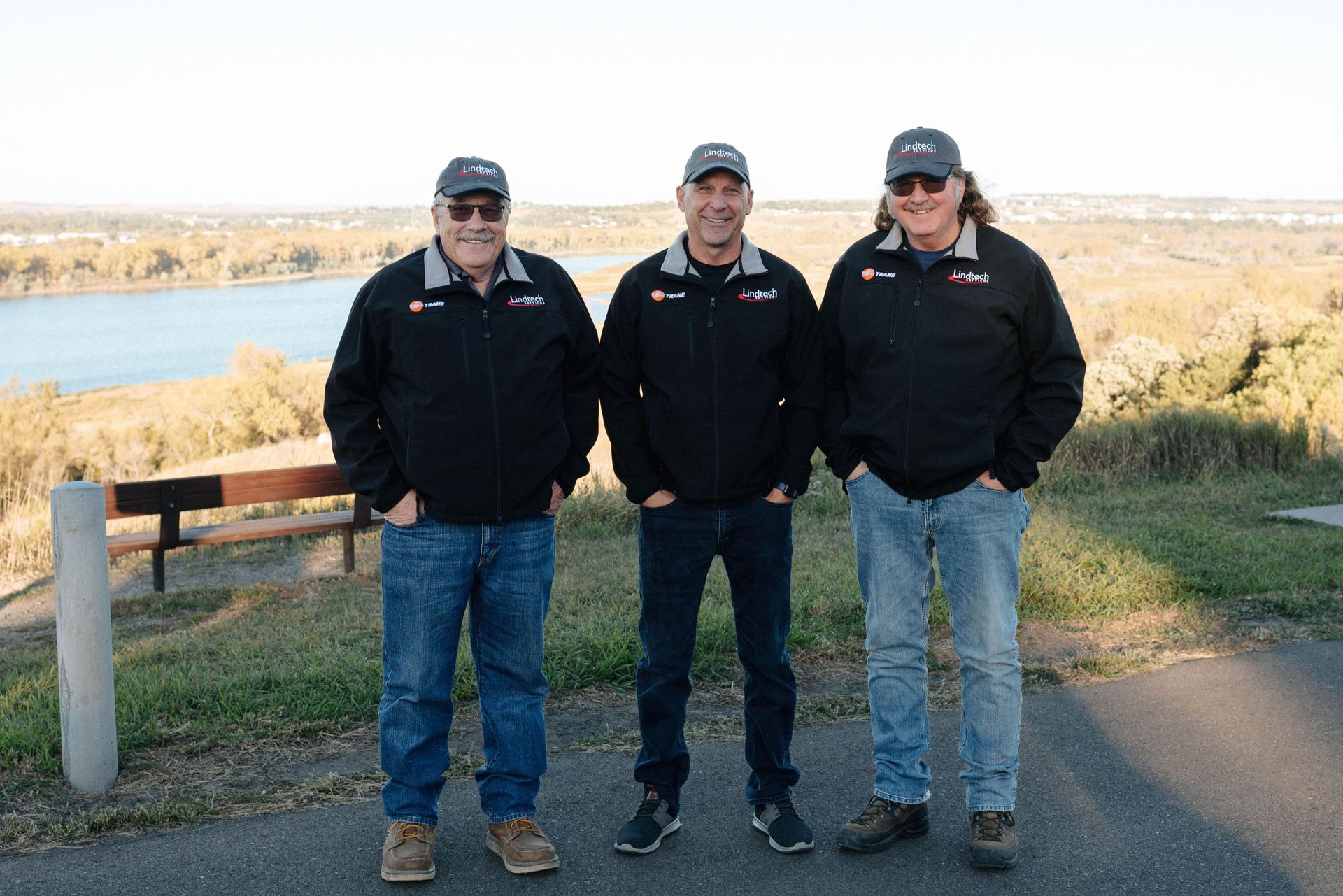 Three men from Lindtech Services, Inc are standing next to each other in front of a lake.