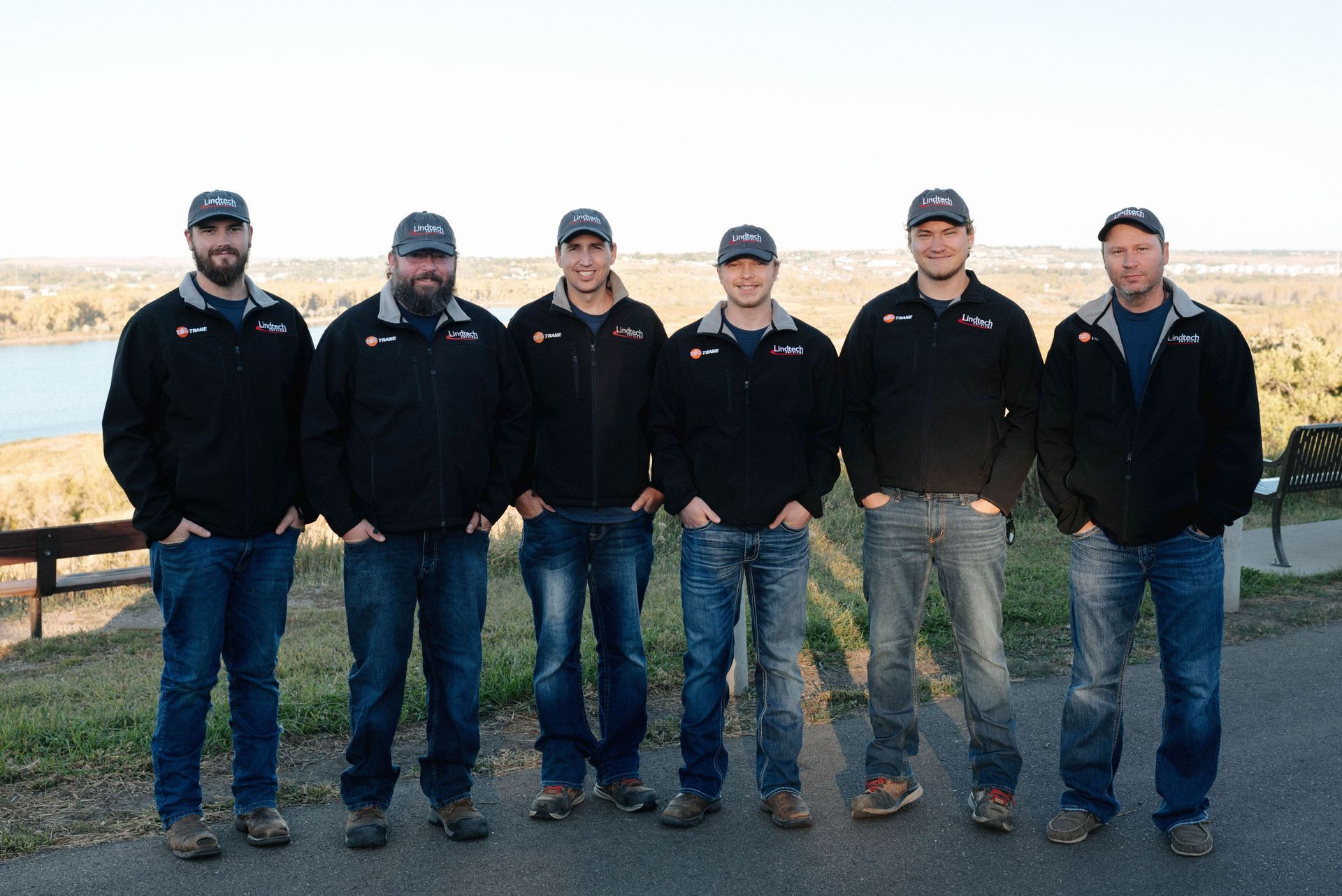 A group of men from Lindtech Services, Inc stands next to each other in front of a lake.