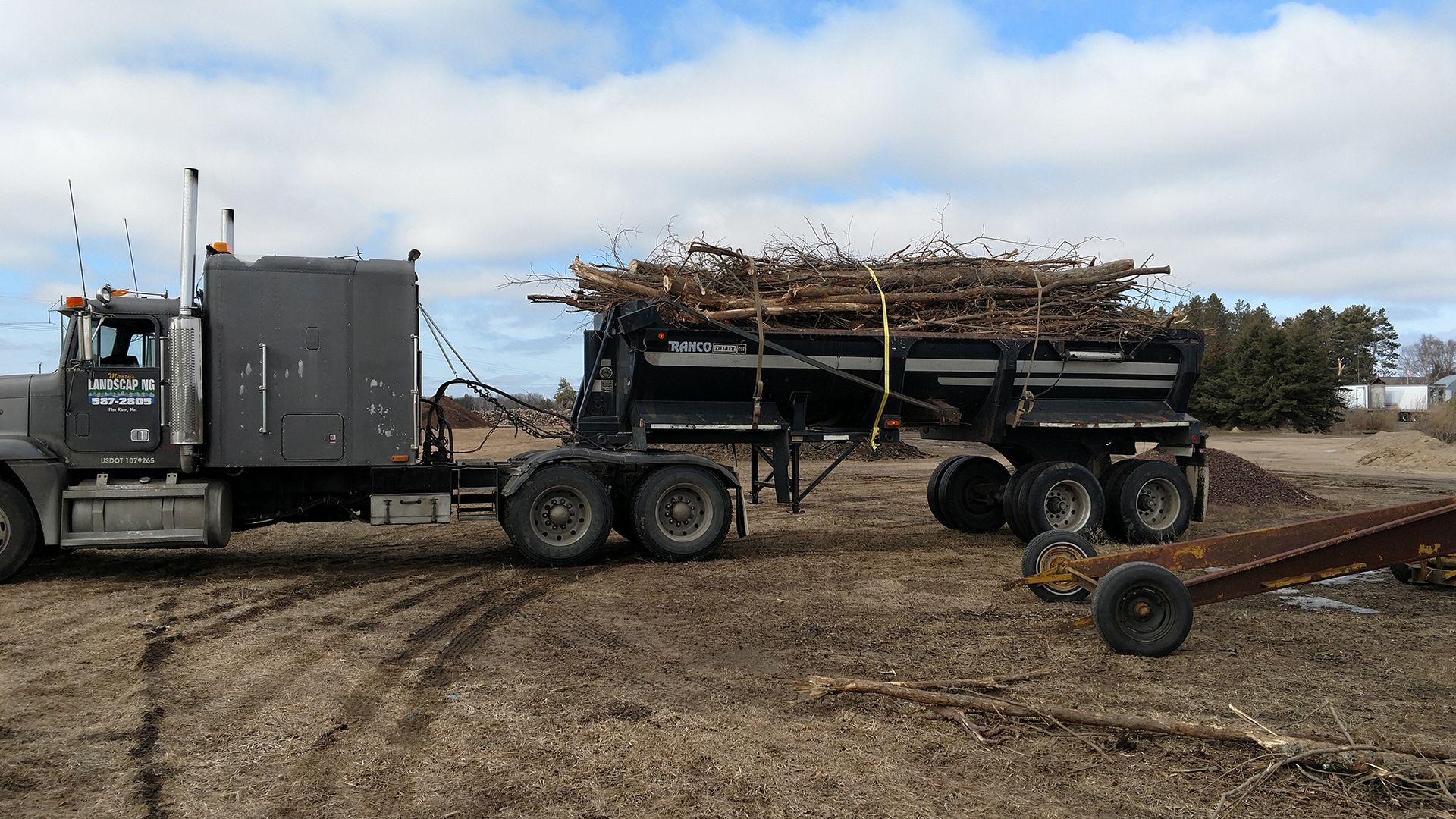 Semi-truck hauling a loaded trailer in a muddy field under a cloudy sky