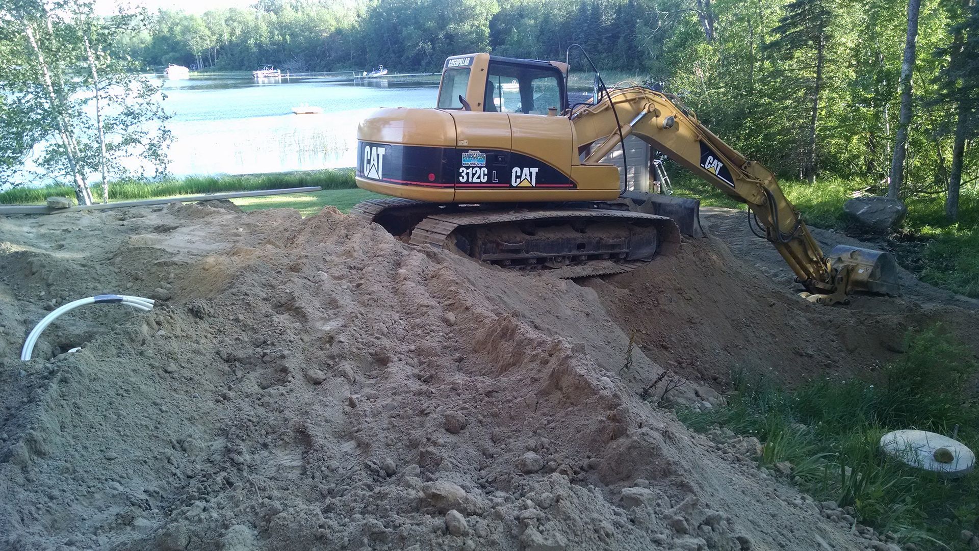 Yellow excavator digging dirt beside a lakeshore in a wooded area