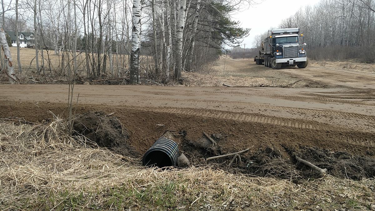 Truck on a muddy dirt road near a culvert in a rural, leafless landscape