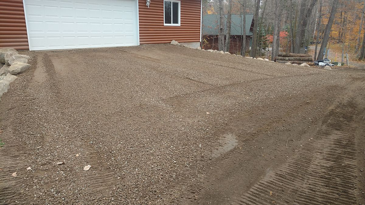 Freshly spread gravel driveway in front of a garage and house siding