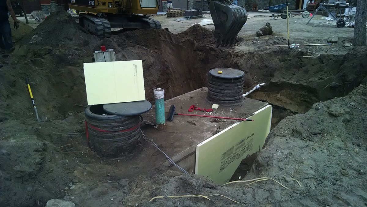 Excavation site with exposed red pipes, concrete cylinders, and dirt trench in a construction area