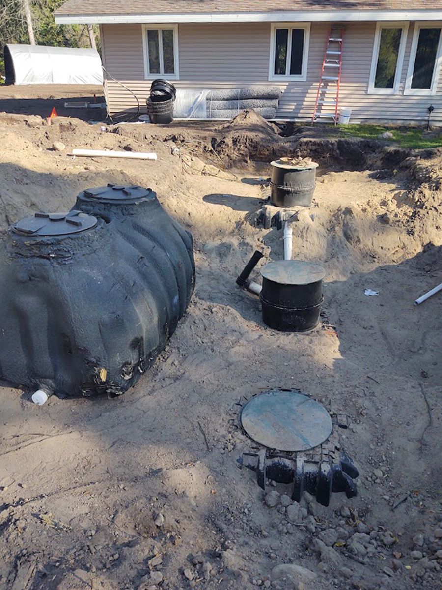 Backyard excavation with large black tank, pipes, and trench near a house foundation