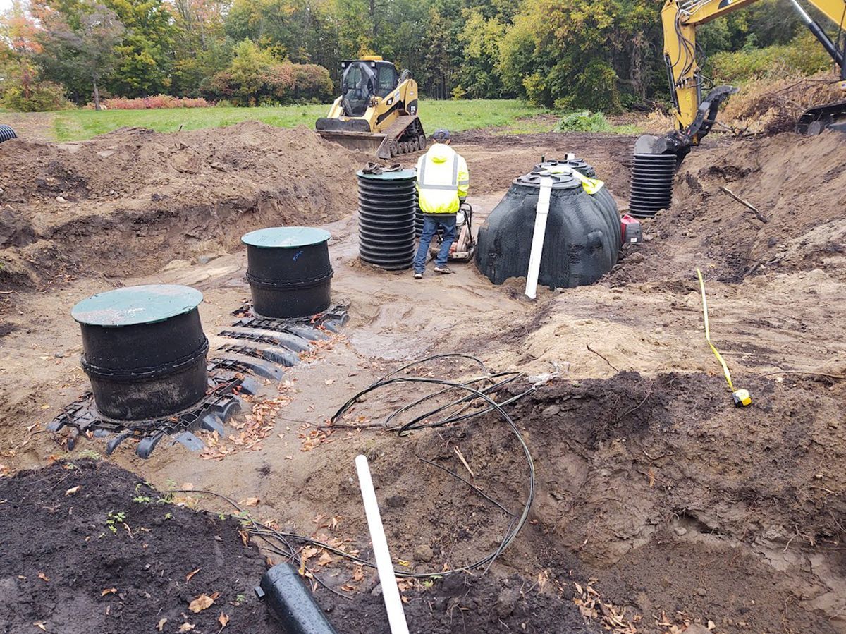 Underground utility installation with black tanks, piping, and workers at a muddy construction site