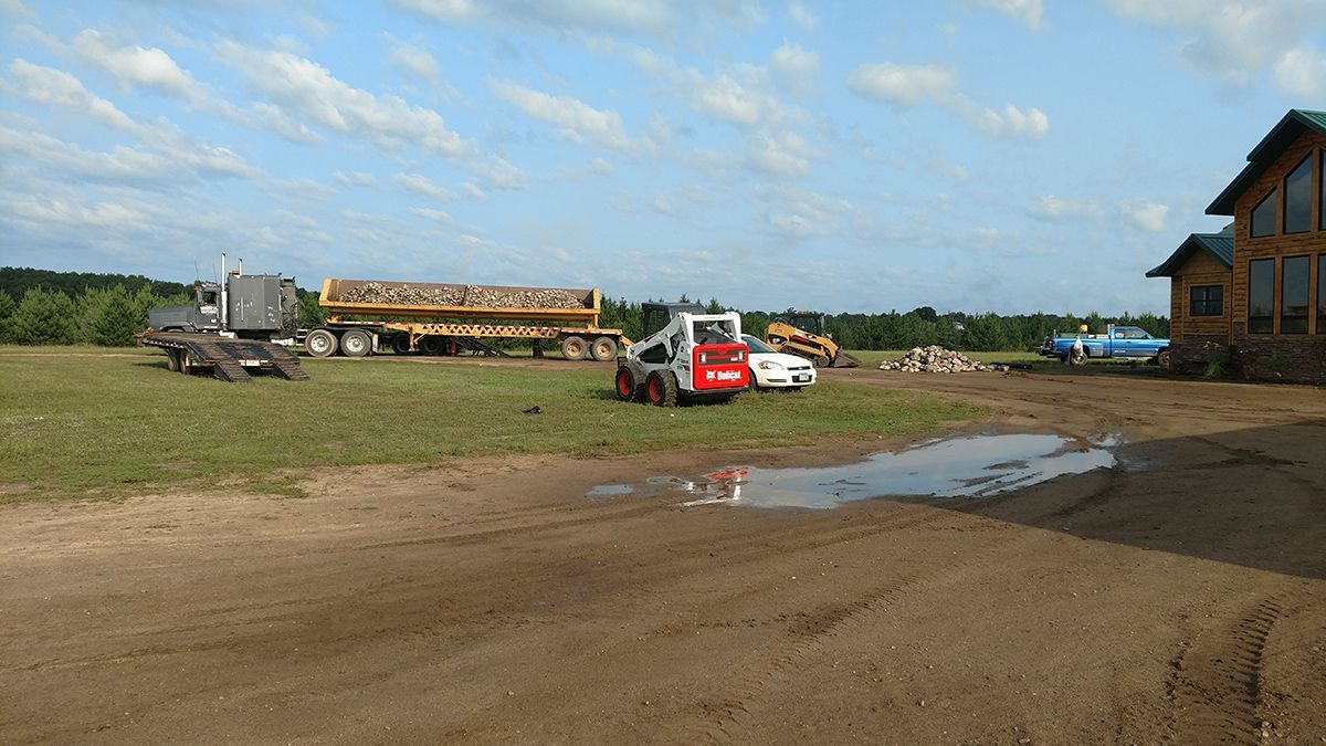 Construction site with trucks and equipment on a muddy dirt lot under a partly cloudy sky