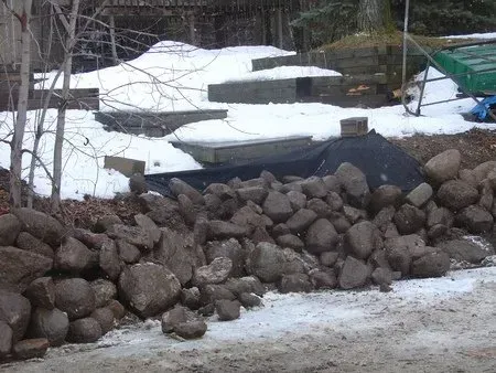 Stacked rocks beside a snowy path, with a dark tarp and winter-covered ground in the background