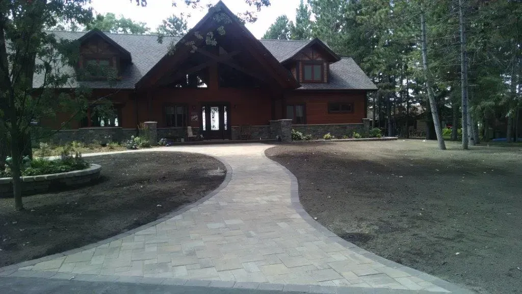Stone path leading to a rustic log cabin surrounded by trees and a wooded yard