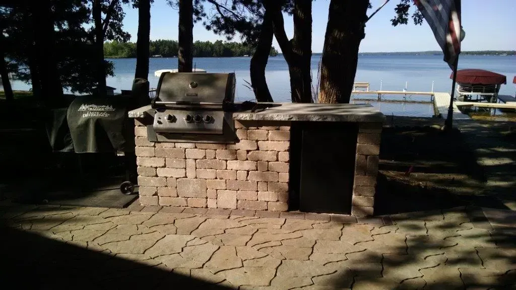 Brick barbecue grill in a shaded lakeside park with trees and benches in the background