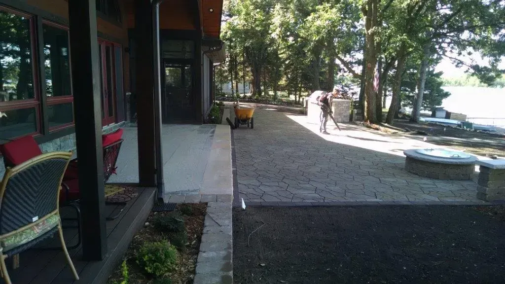 Lakeside patio and gravel path with trees, benches, and a person walking in the distance