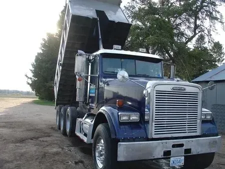 Blue dump truck with raised bed parked on a rural road