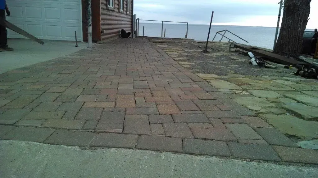 Brick walkway beside a waterfront with a bench, railing, and houses on the left