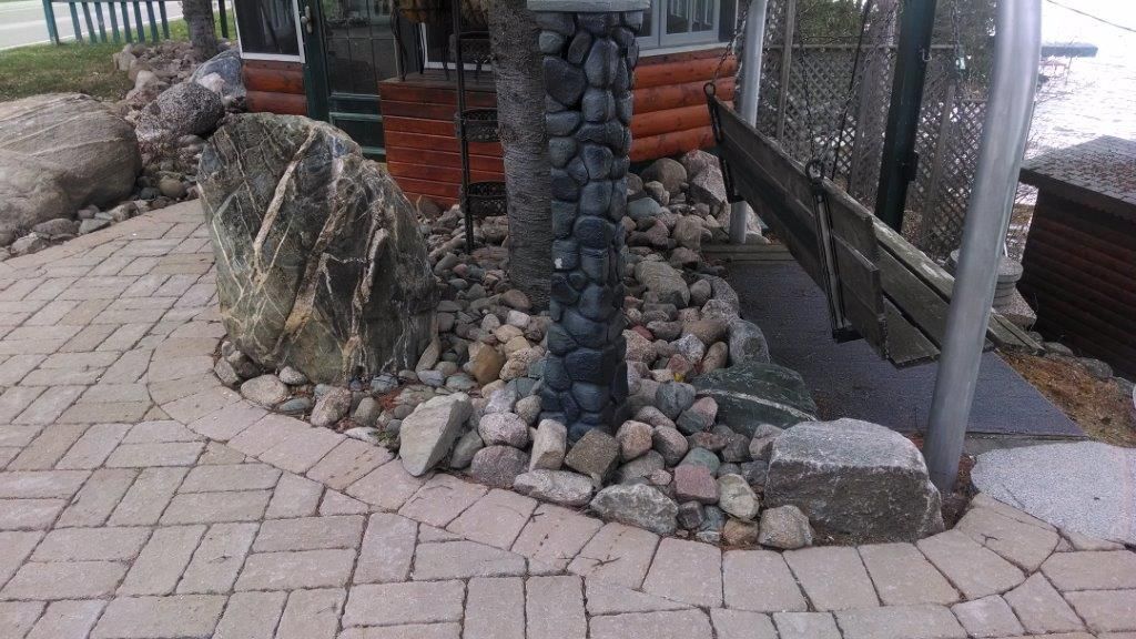 Stone-and-brick landscaped path beside a building with rocks, timber posts, and a fenced walkway