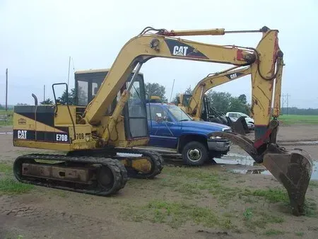 Yellow CAT excavator digging beside a blue pickup truck on muddy ground outdoors