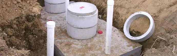 Outdoor construction site with concrete foundation, white PVC pipes, and a circular drain opening.