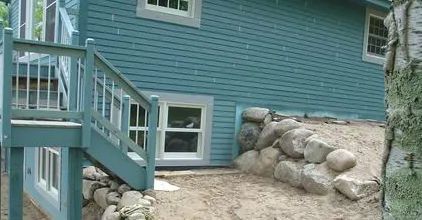Blue house exterior with wooden stairs and large rocks along the foundation