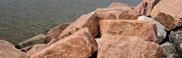 Large tan rocks piled along a shoreline beside calm water