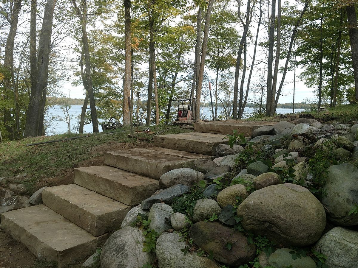 Stone steps leading through a wooded lakeside area with rocks and trees.