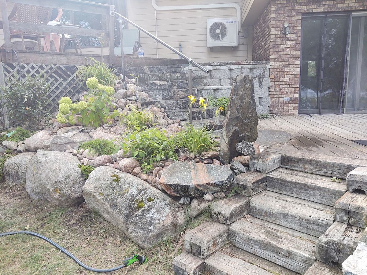 Stone steps beside a rock garden and shrubbery, leading to a building entrance with a black door