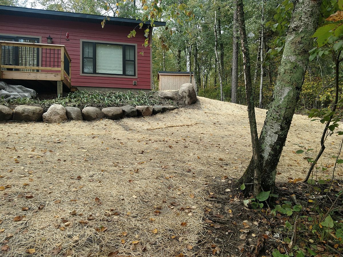 Red cabin with stone border beside a leaf-covered yard in a wooded area
