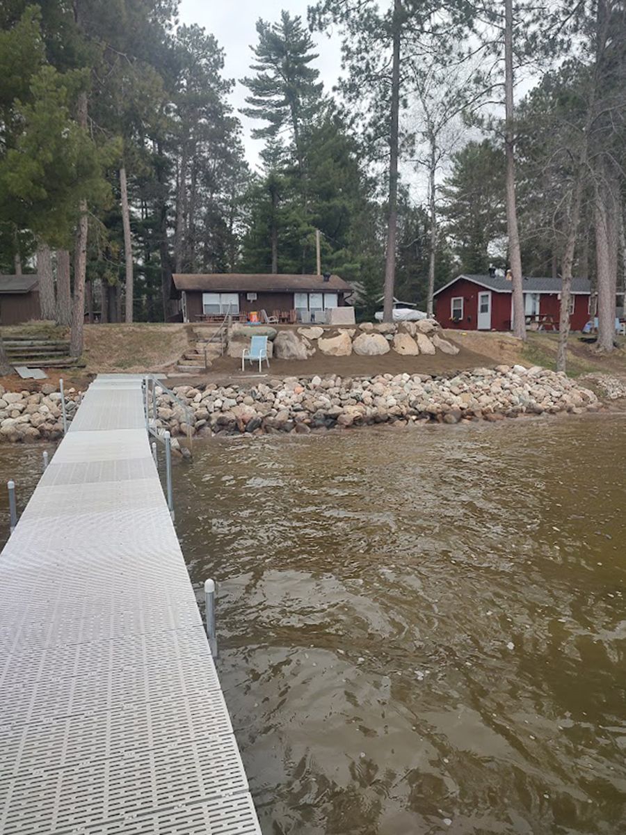 Floating dock leading to a lakeside cabin and red boathouse among pine trees