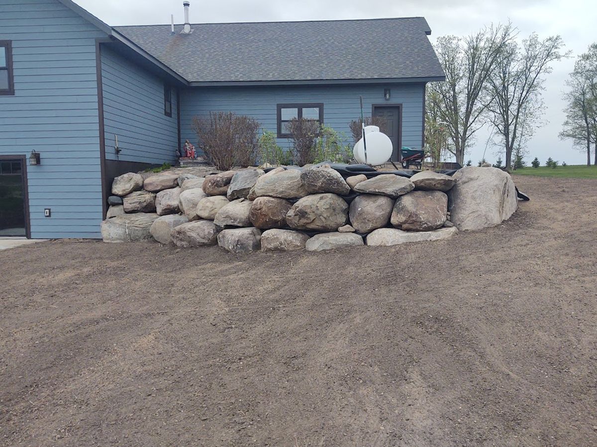 Blue house with a large stone retaining wall and a white satellite dish in a rural yard